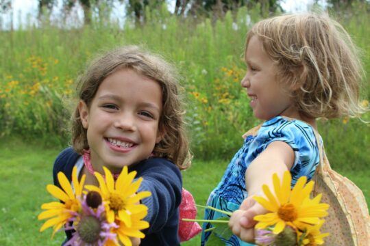 Two children are holding prairie flowers and smiling.