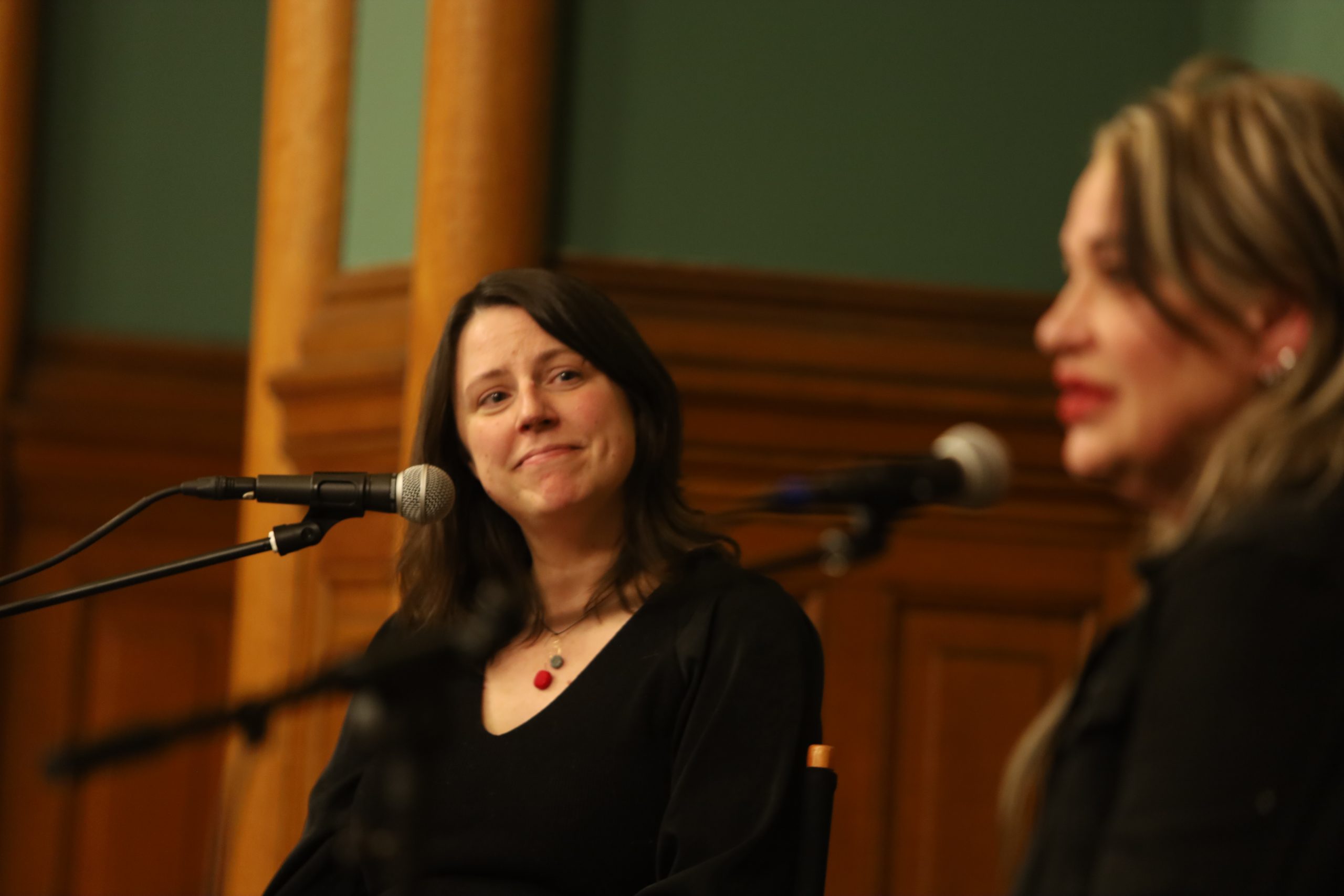 Andrea Swensson (left) smiling at Mary Lucia (right) on stage with microphones for each.